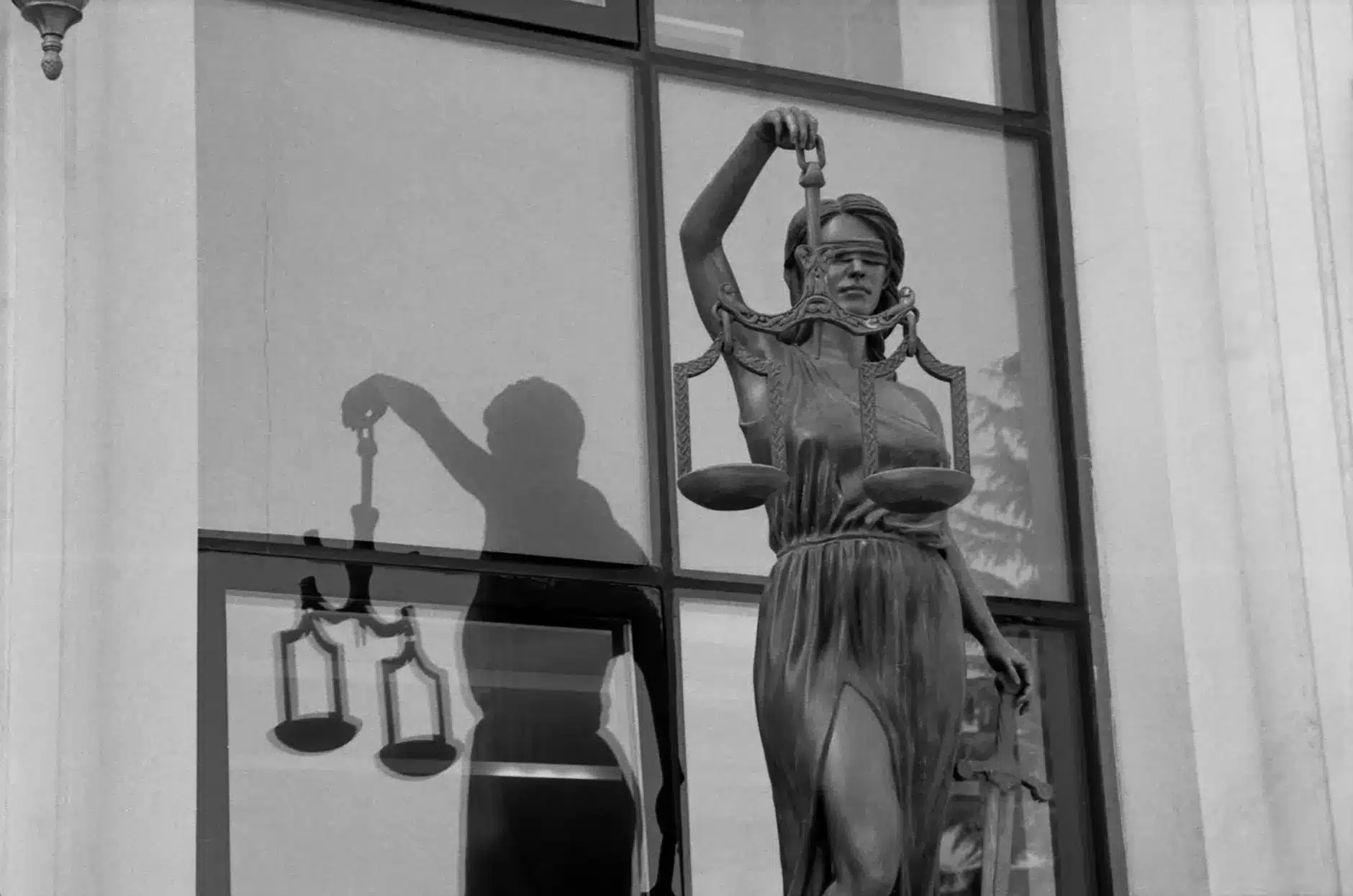 Statue of Lady Justice holding scales in front of a window.