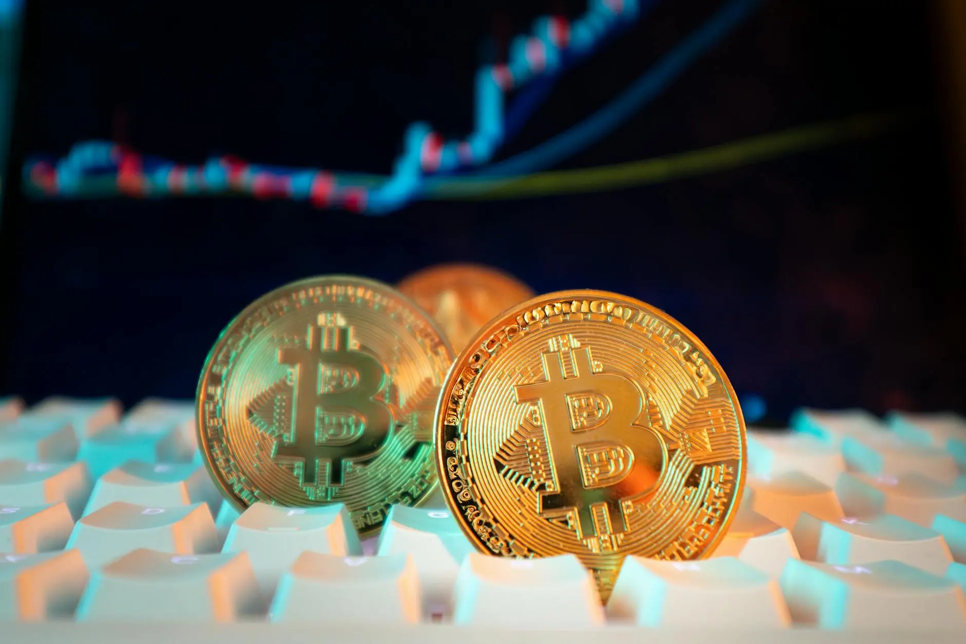 Close-up of Bitcoin coins on a keyboard with a digital market chart in the background.