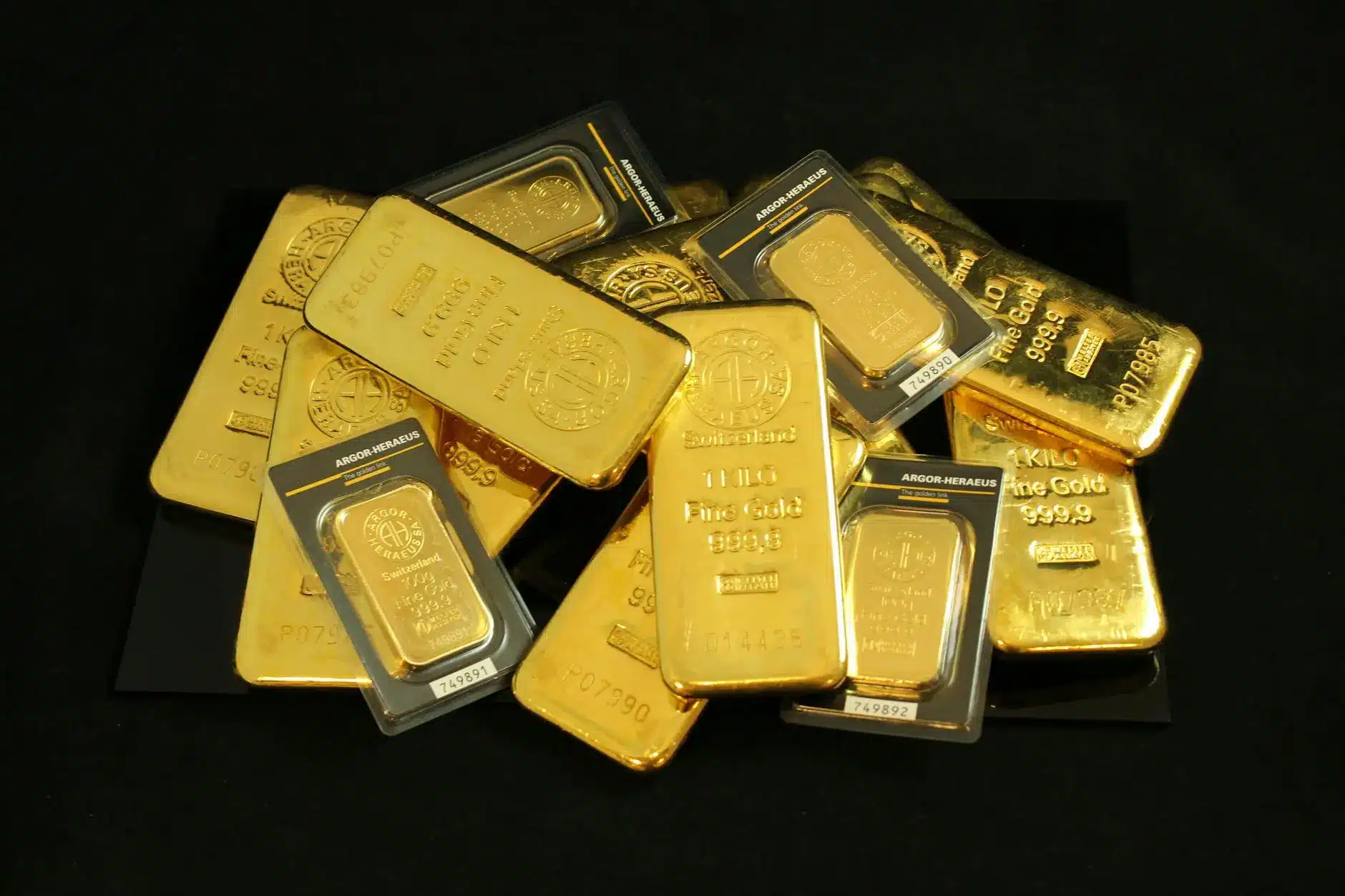 A collection of gold bars and gold bullion in various sizes on a black background.