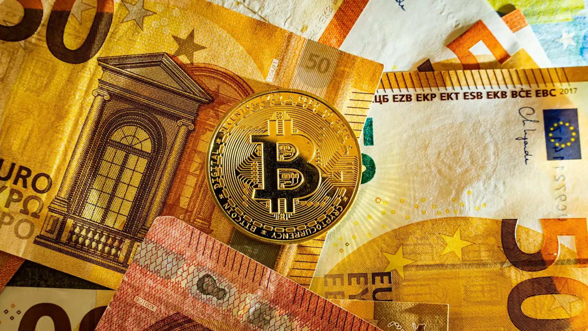 A Bitcoin laid on top of various Euro banknotes.
