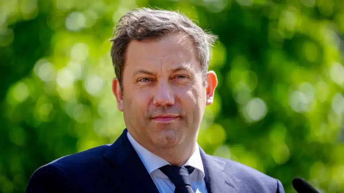 Lars Klingbeil stands outdoors with a green blurred background, dressed in a suit.