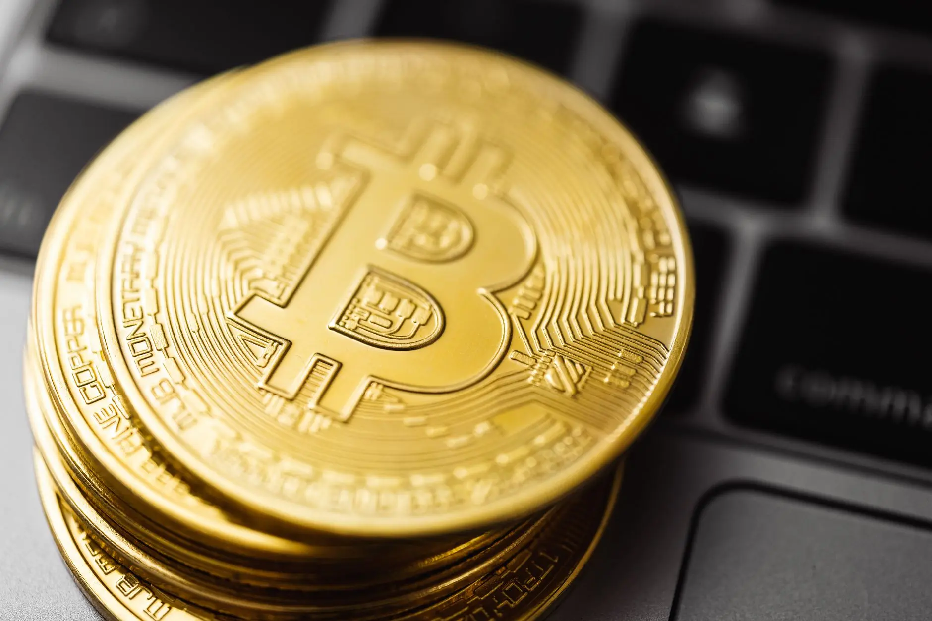 Close-up of a stack of gold Bitcoin coins on a laptop keyboard.