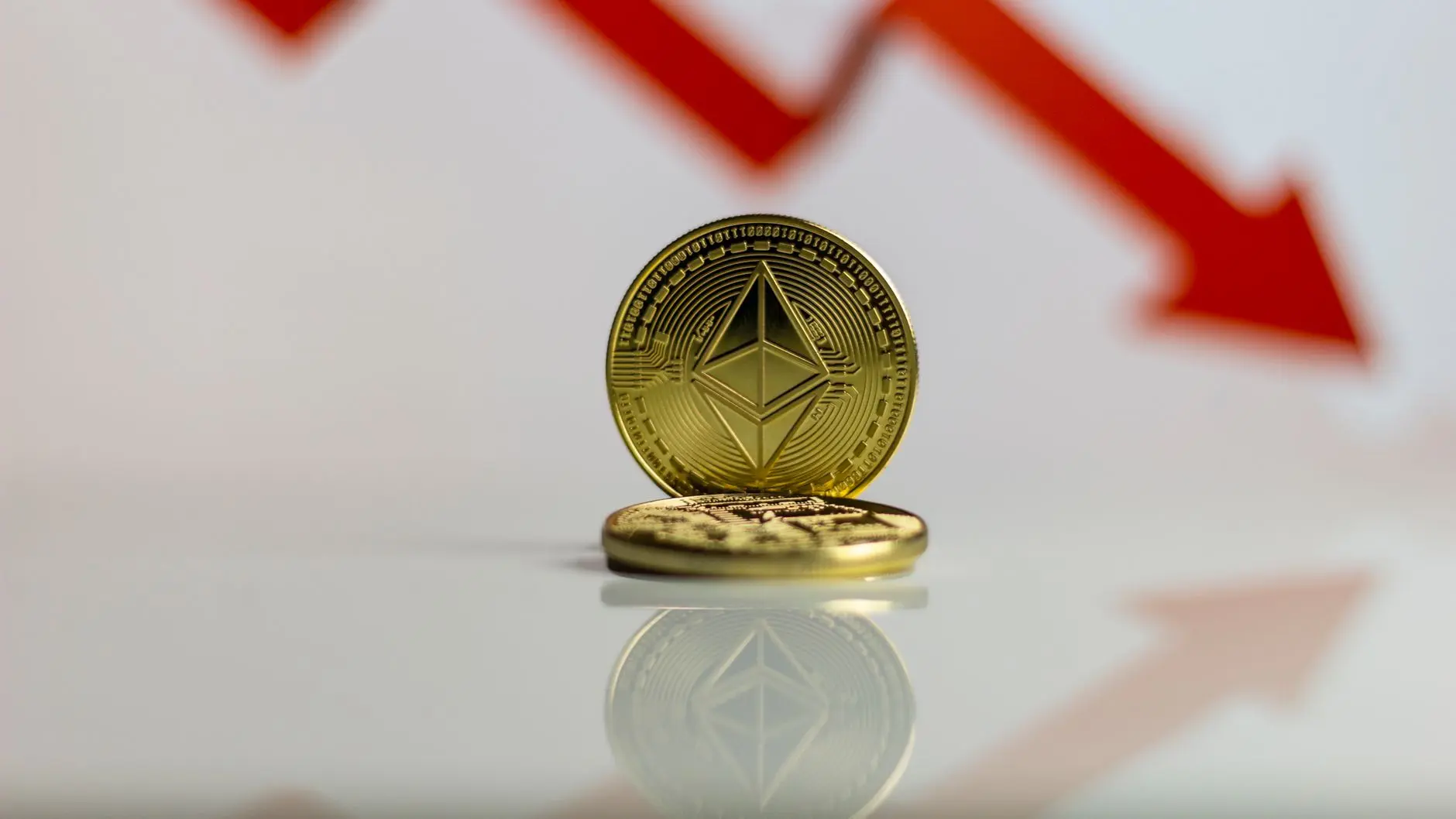 Two Ethereum coins with a downward red arrow in the background, symbolizing market decline.