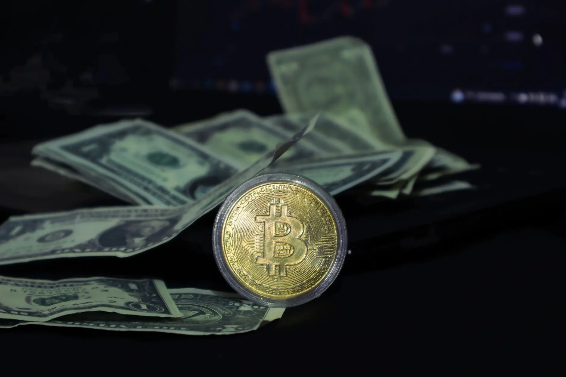 Bitcoin coin placed on scattered US dollar bills with a dark background.