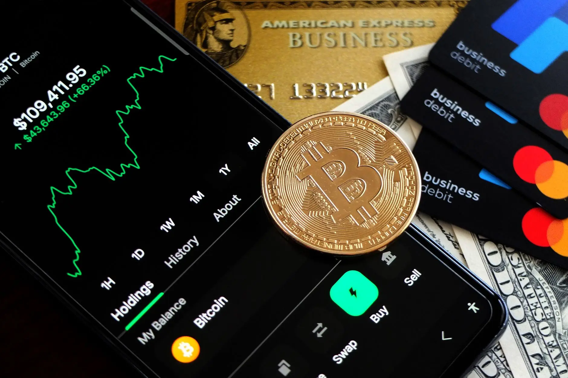 Smartphone displaying Bitcoin value beside debit cards and cash.