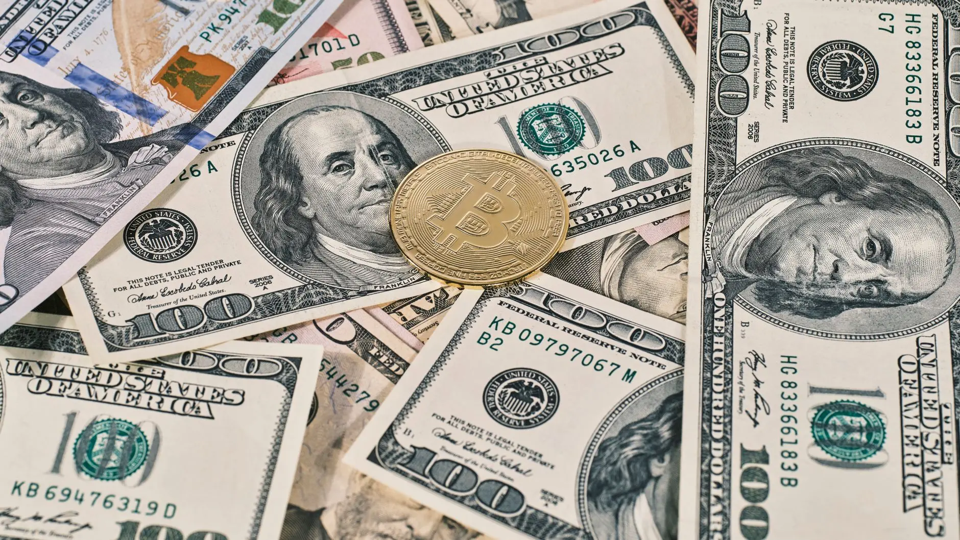 A physical Bitcoin coin placed on various denominations of U.S. dollar bills.