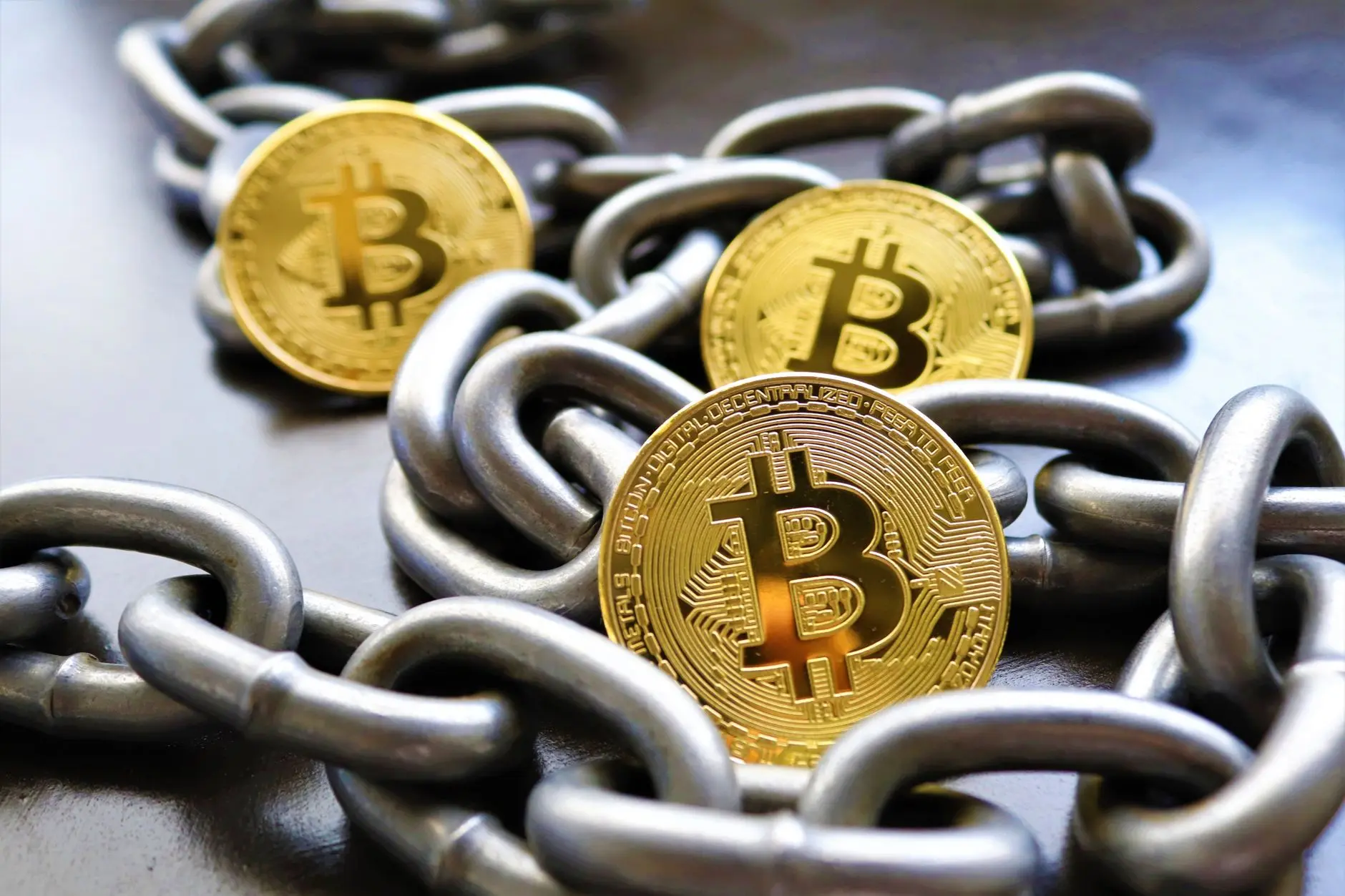 Three gold Bitcoin coins resting on a metal chain.