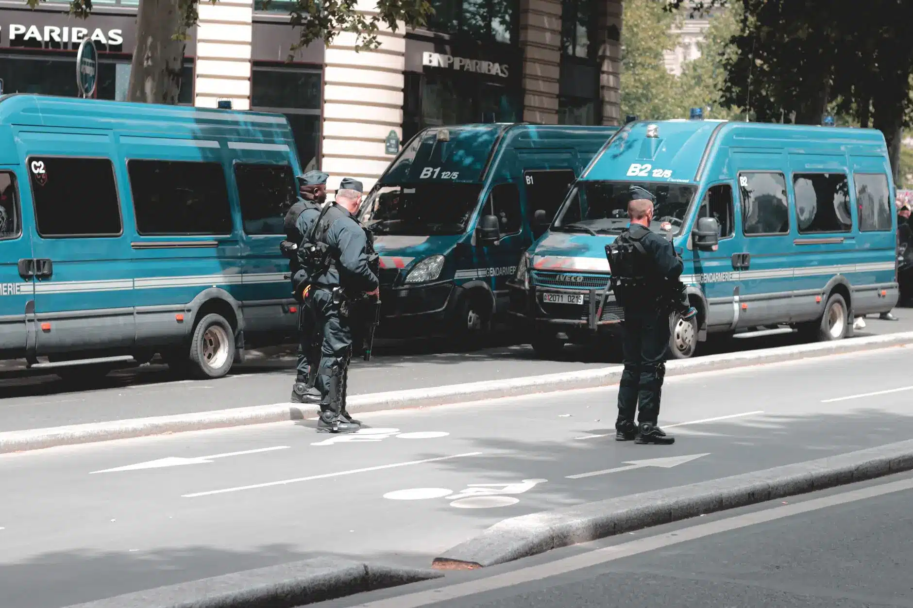 Two French police officers near parked blue police vans in an urban setting.