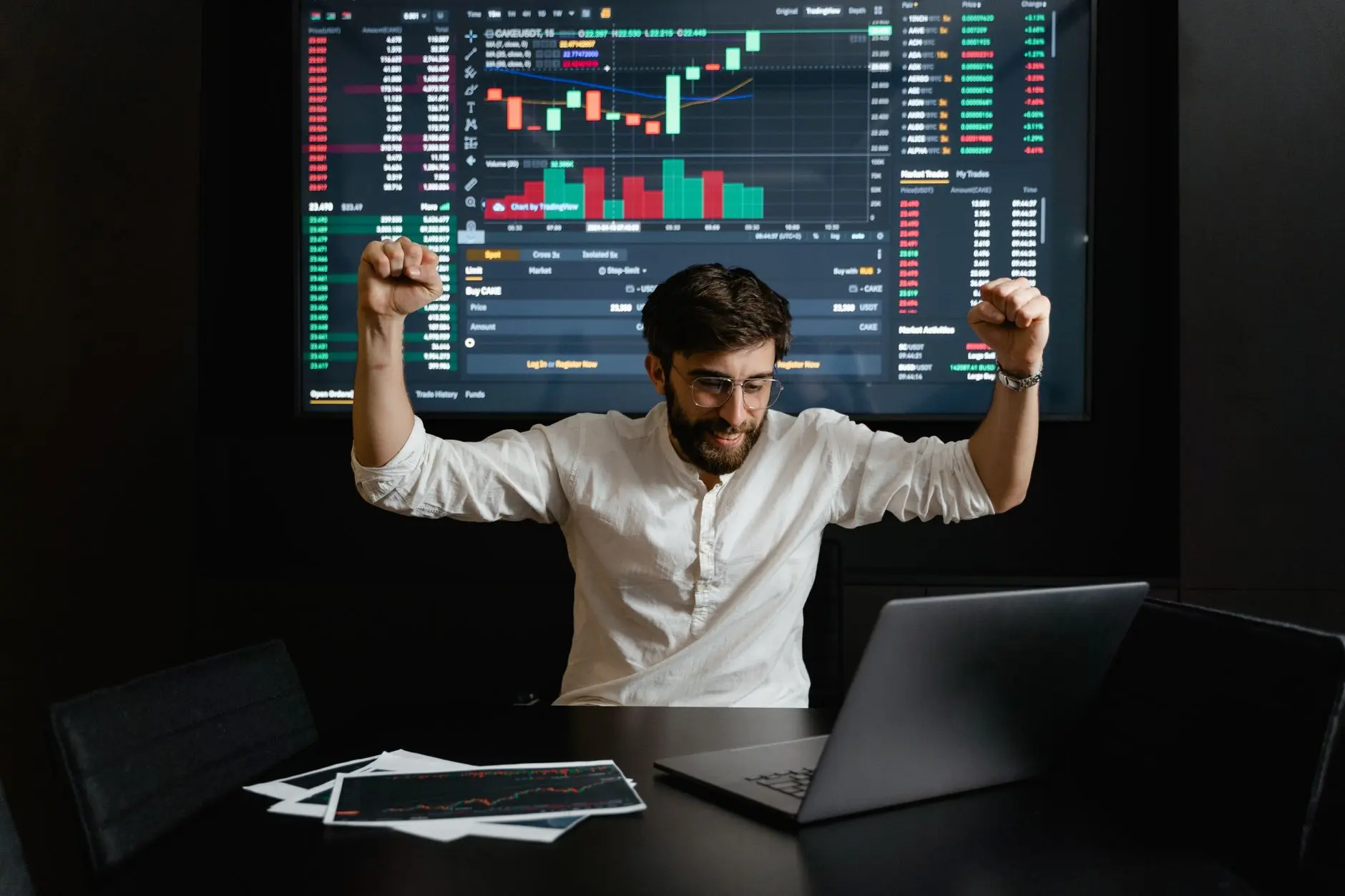 A trader celebrating a successful trade in front of financial charts on a screen.