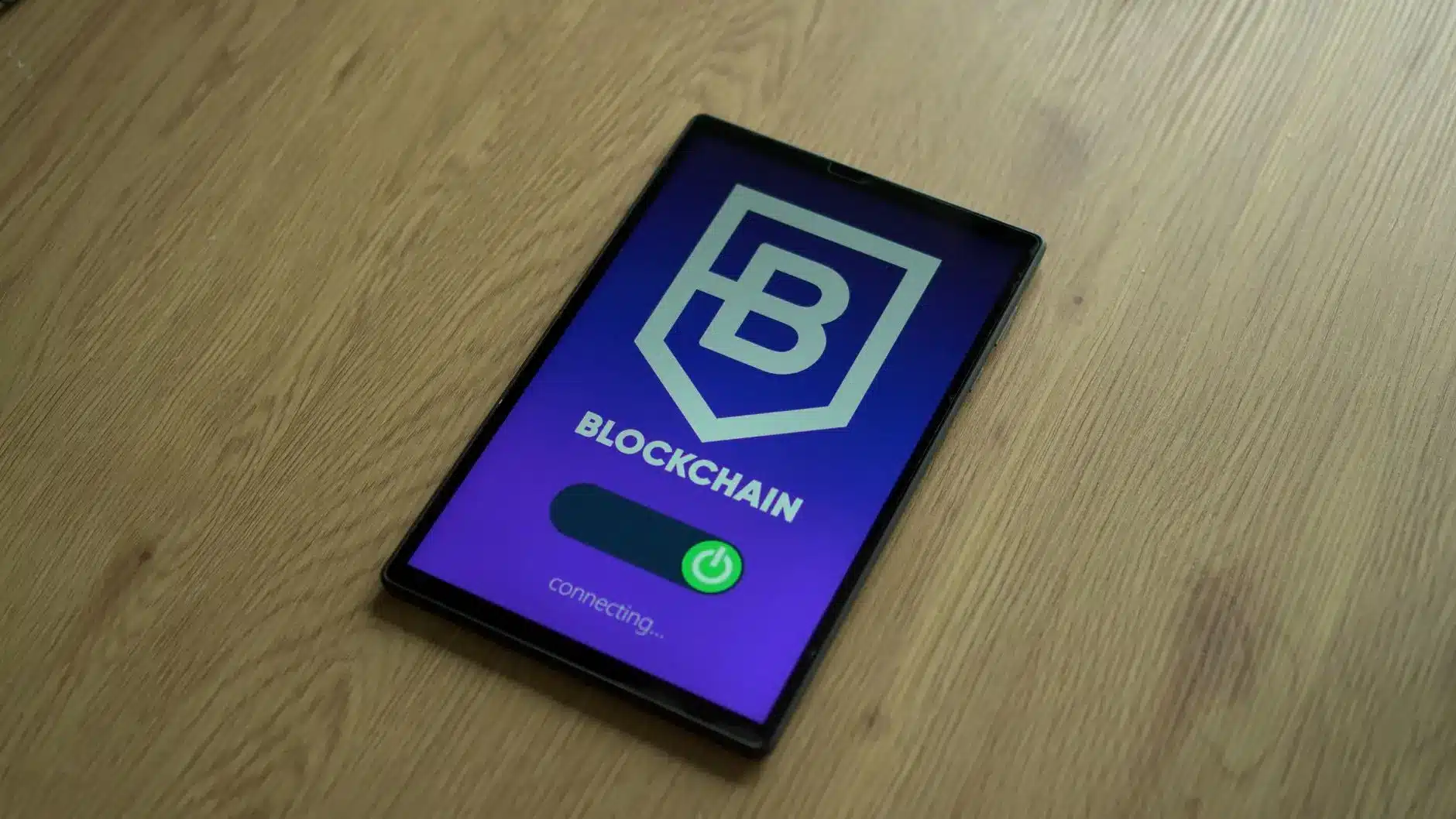 Tablet displaying a blockchain logo and connection status on a wooden surface.