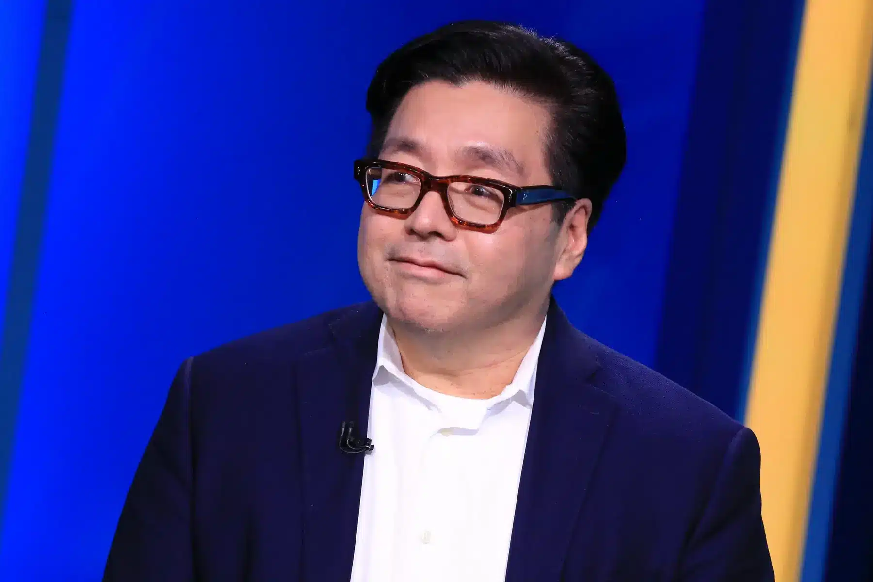 A man in glasses wearing a navy blazer against a blue background.