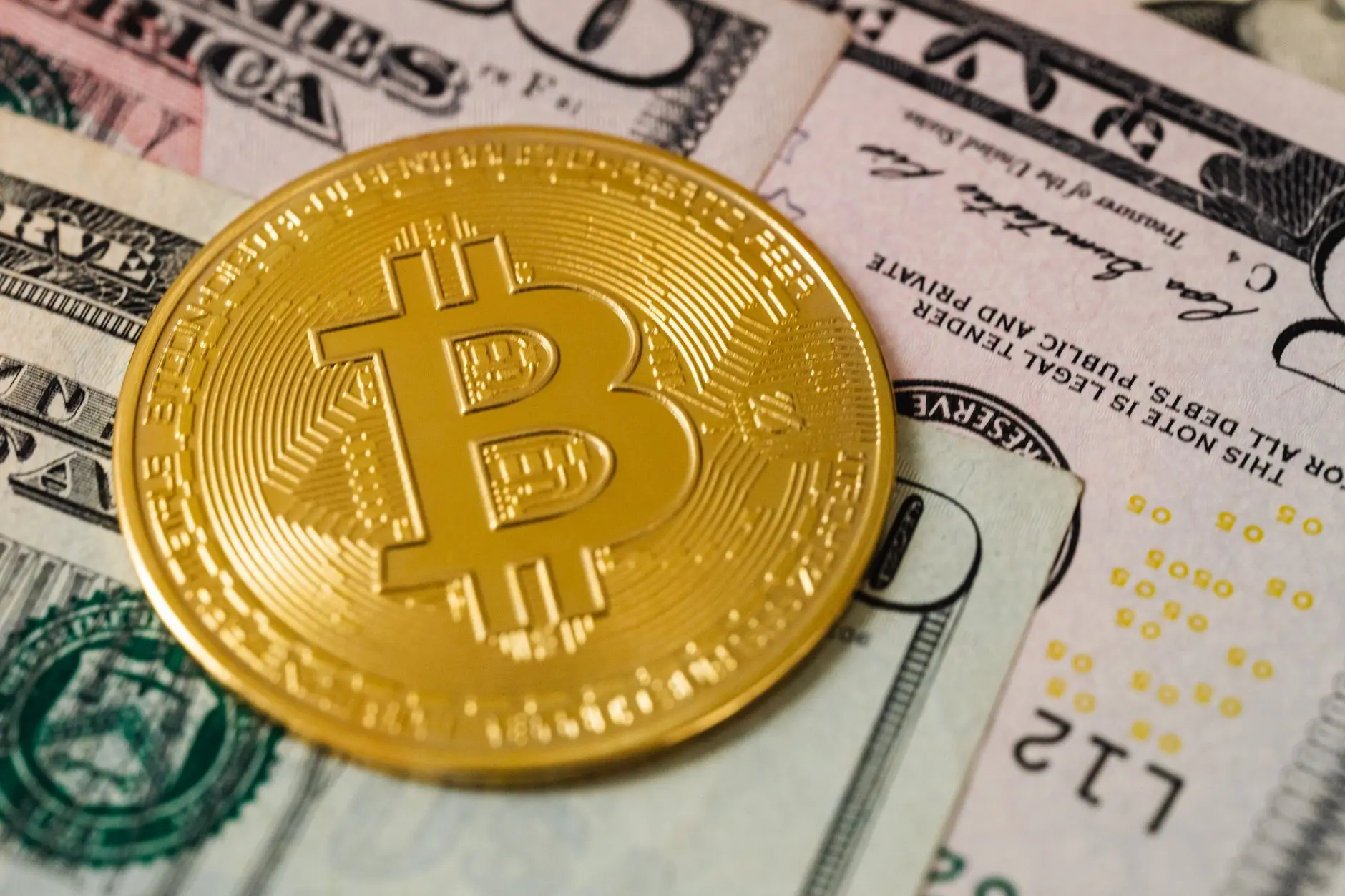 A gold Bitcoin coin placed on US dollar bills.