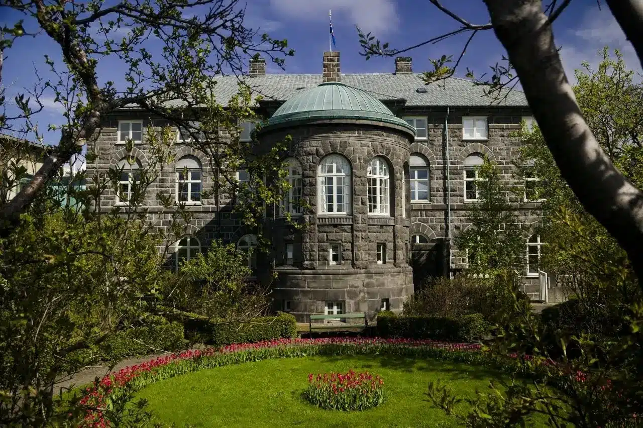 Exterior view of the Althingi parliament building in Reykjavik, featuring grey stone walls and a green dome.