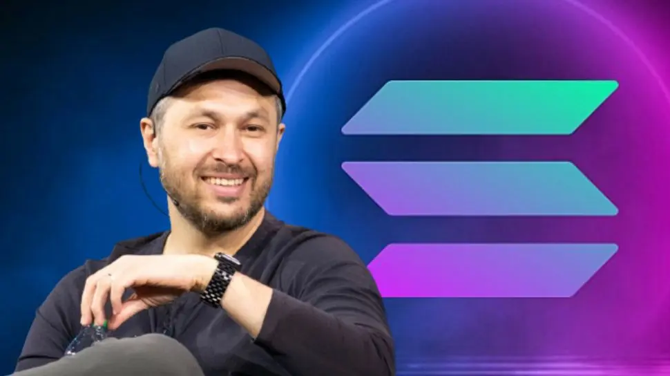 Anatoly Yakovenko wearing a black cap and shirt, smiling in front of a large Solana logo background