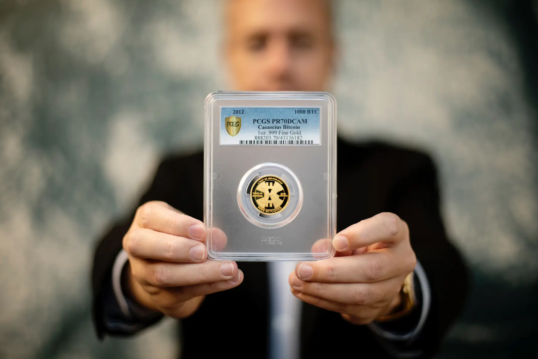 A person holding a PCGS graded 1oz .999 fine gold Casacius Bitcoin coin in a plastic protective slab