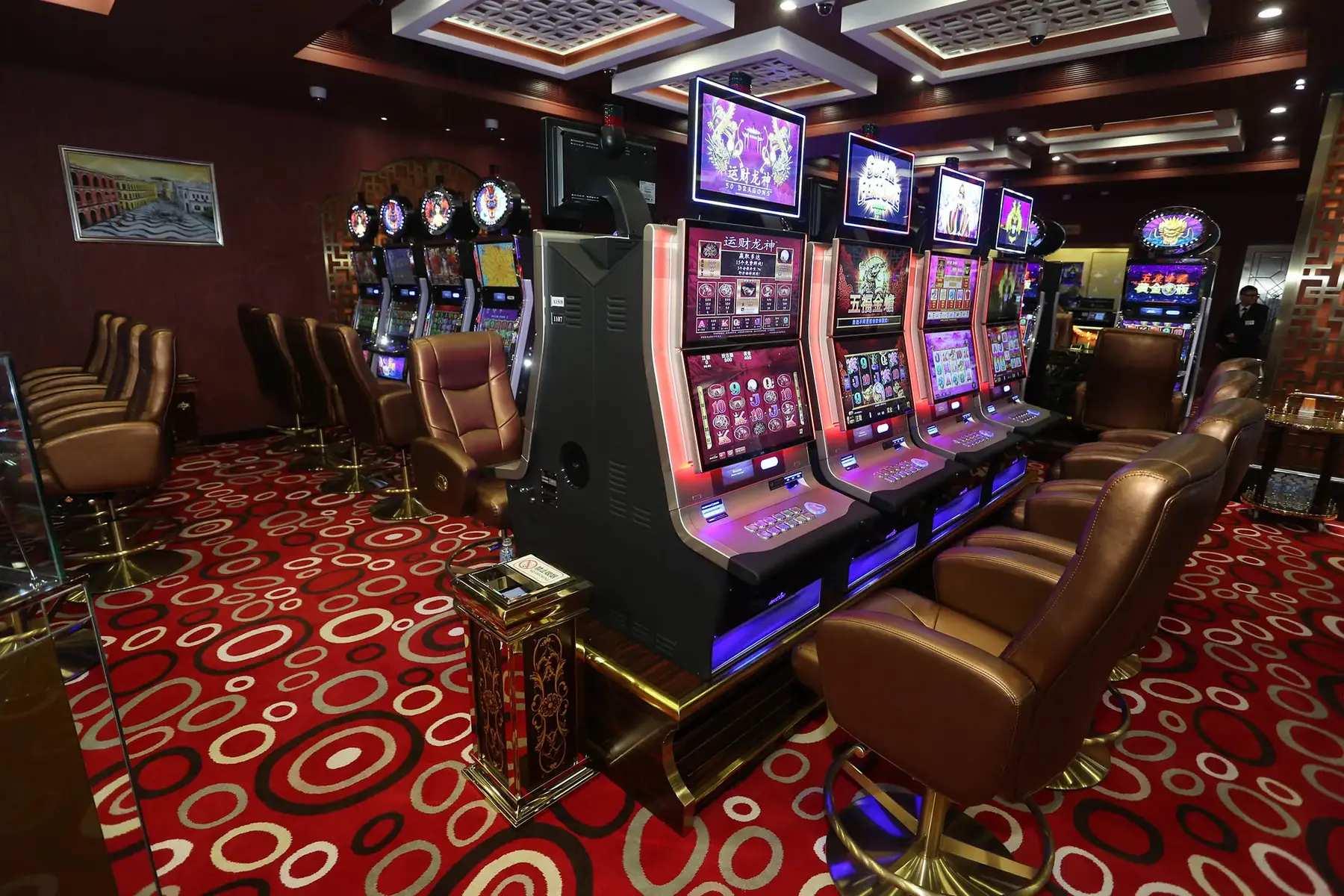 A row of modern electronic slot machines with bright displays and brown leather seats in a casino room