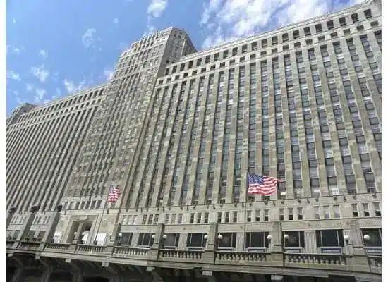 Low-angle exterior view of the Chicago Mercantile Exchange building under a blue sky with American flags.