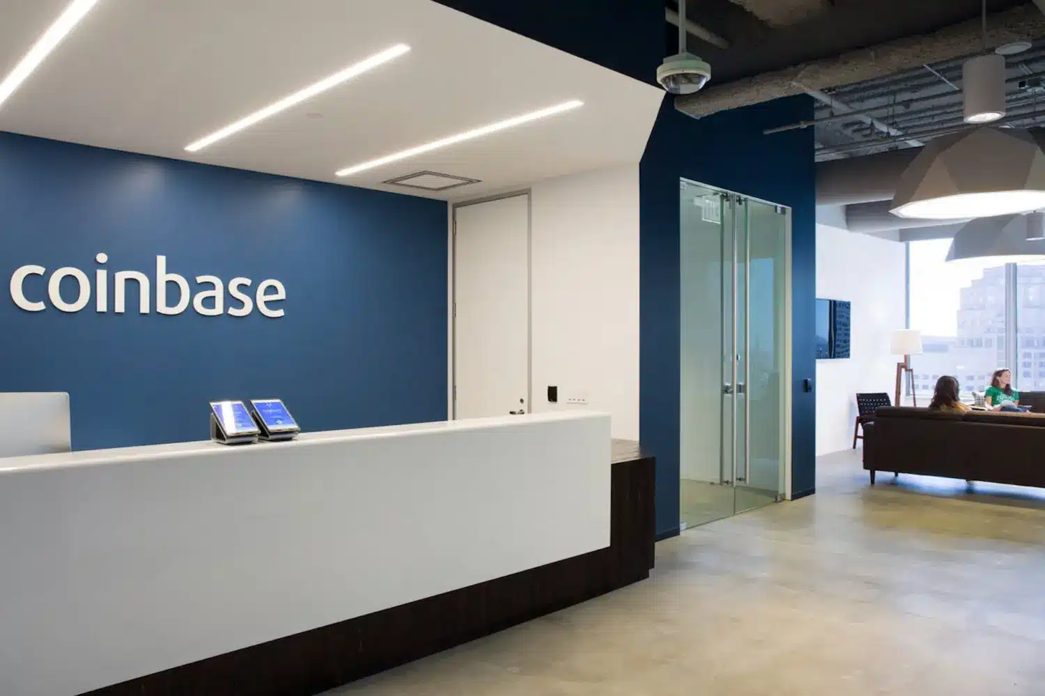 Modern reception area of Coinbase office featuring a white desk and blue wall with the Coinbase logo