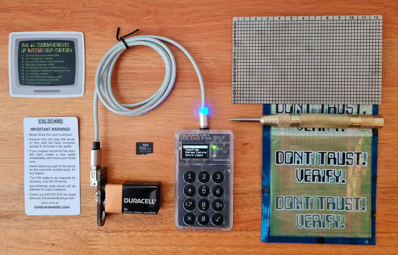Coldcard hardware wallet on a wooden table with a seed backup card, battery, and security checklist.