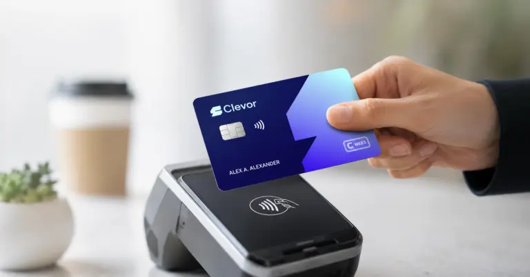 A hand holding a navy blue Clevor Web3 crypto debit card over a contactless payment terminal.