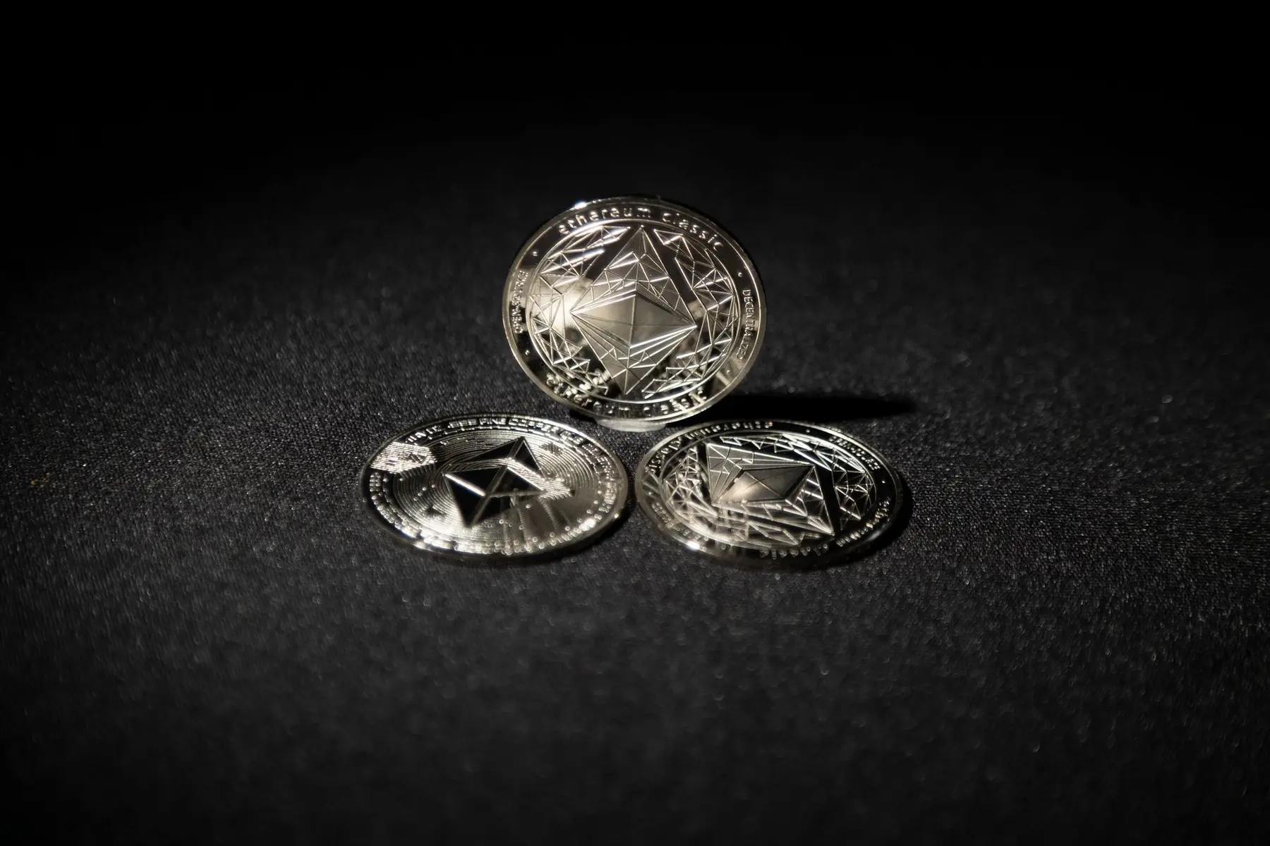 Three silver physical Ethereum coins with the diamond-shaped logo resting on a black surface