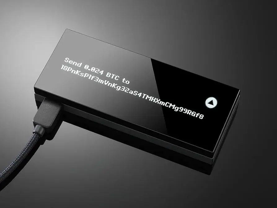 A black hardware cryptocurrency wallet connected by a USB cable showing a BTC transaction address on its screen
