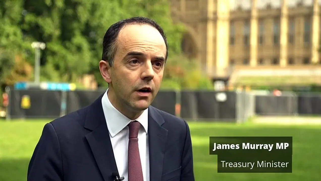 James Murray MP, Treasury Minister, wearing a suit and tie in front of the Palace of Westminster.