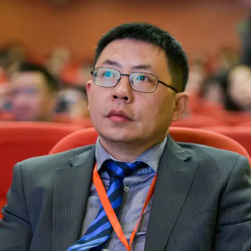 Portrait of Kevin Zhang wearing a grey suit, blue striped tie, and glasses at a conference.