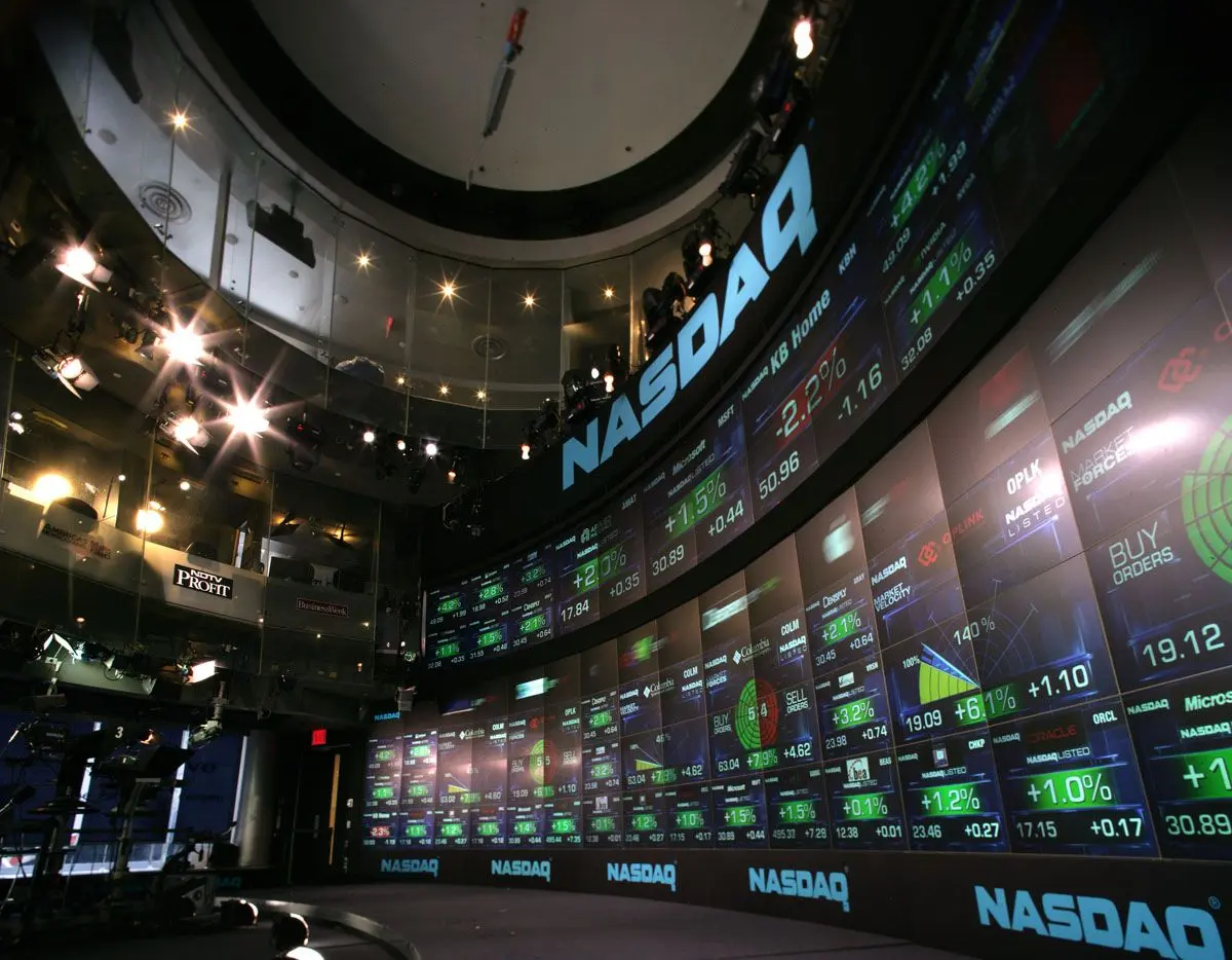 Wide shot of the Nasdaq MarketSite trading floor with large curved digital displays showing stock market data.