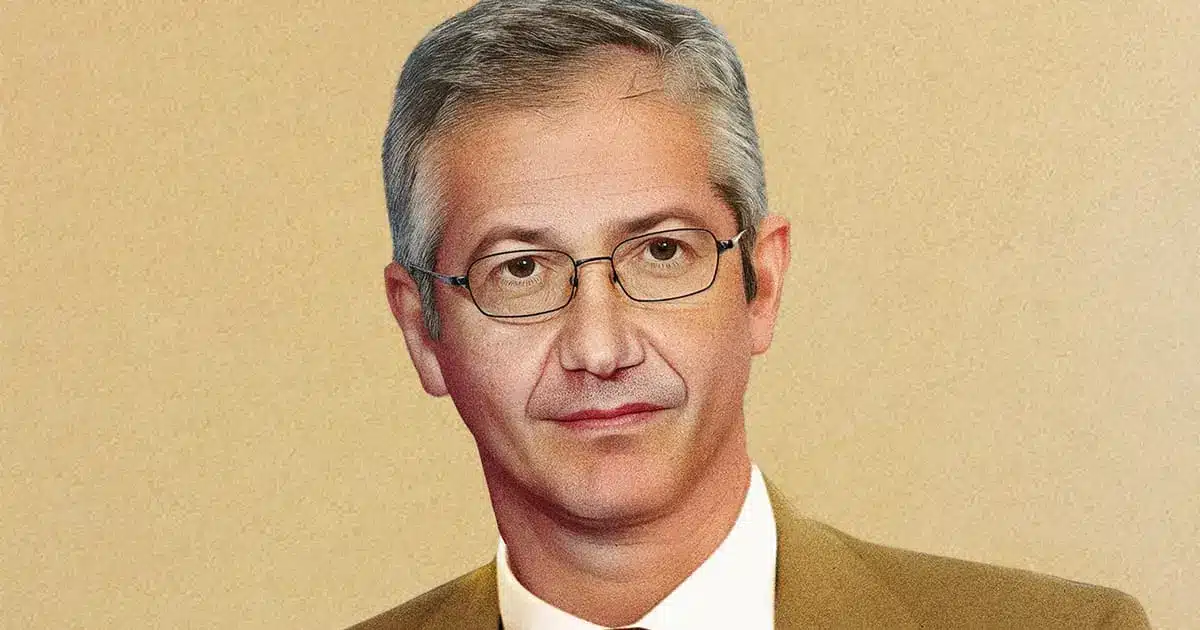 Portrait of Pablo Hernandez de Cos wearing glasses and a tan suit jacket against a textured beige background