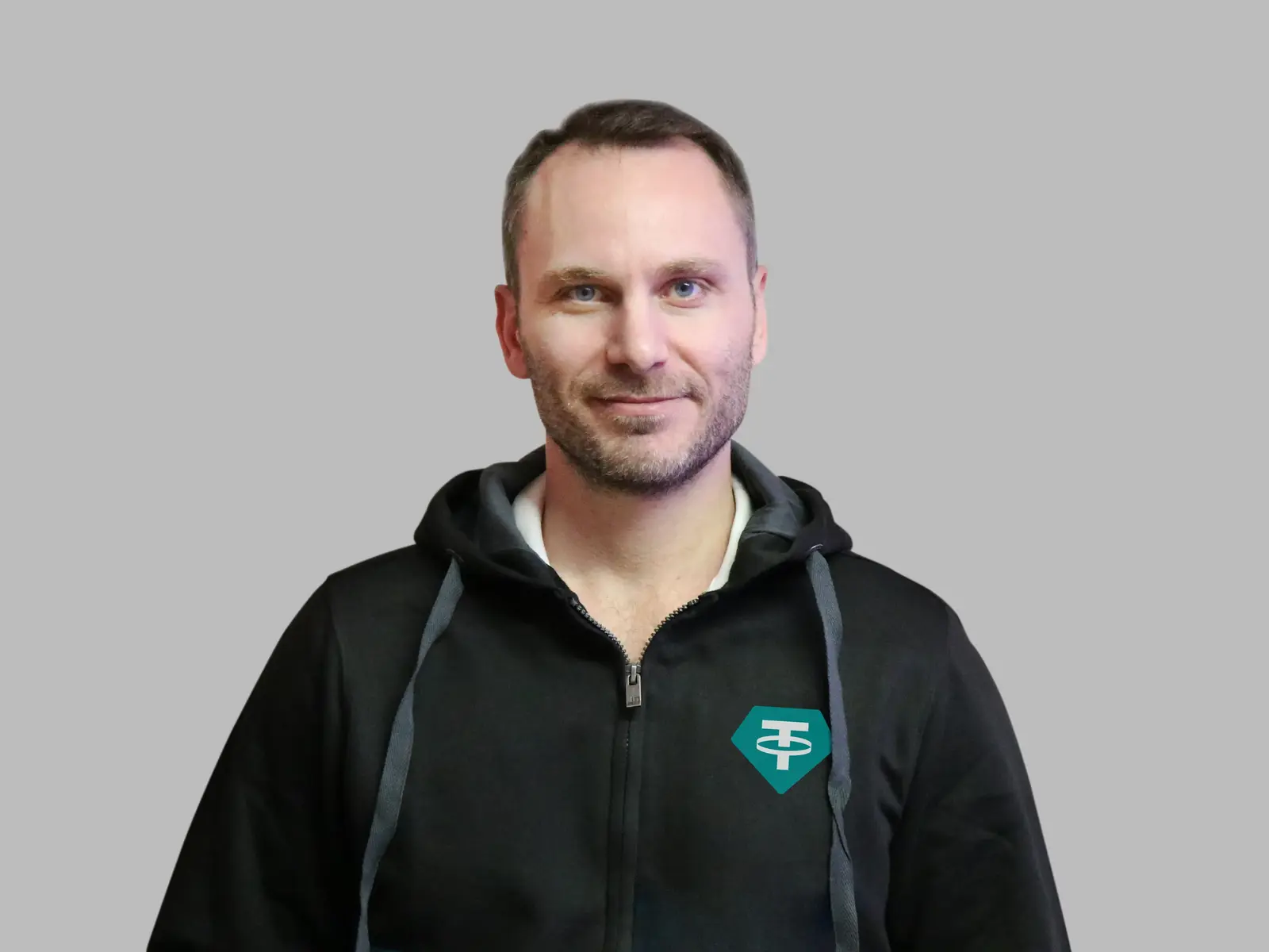 Paolo Ardoino wearing a black hoodie with the Tether logo on the chest against a grey background