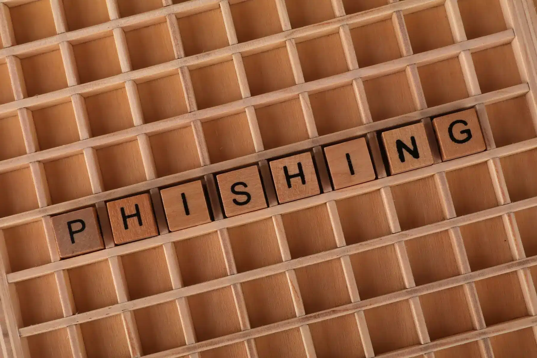 Wooden blocks spelling the word PHISHING arranged in a wooden grid tray