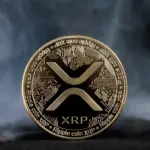 A gold-colored physical XRP token with a circuit board pattern, set against a smoky dark background.