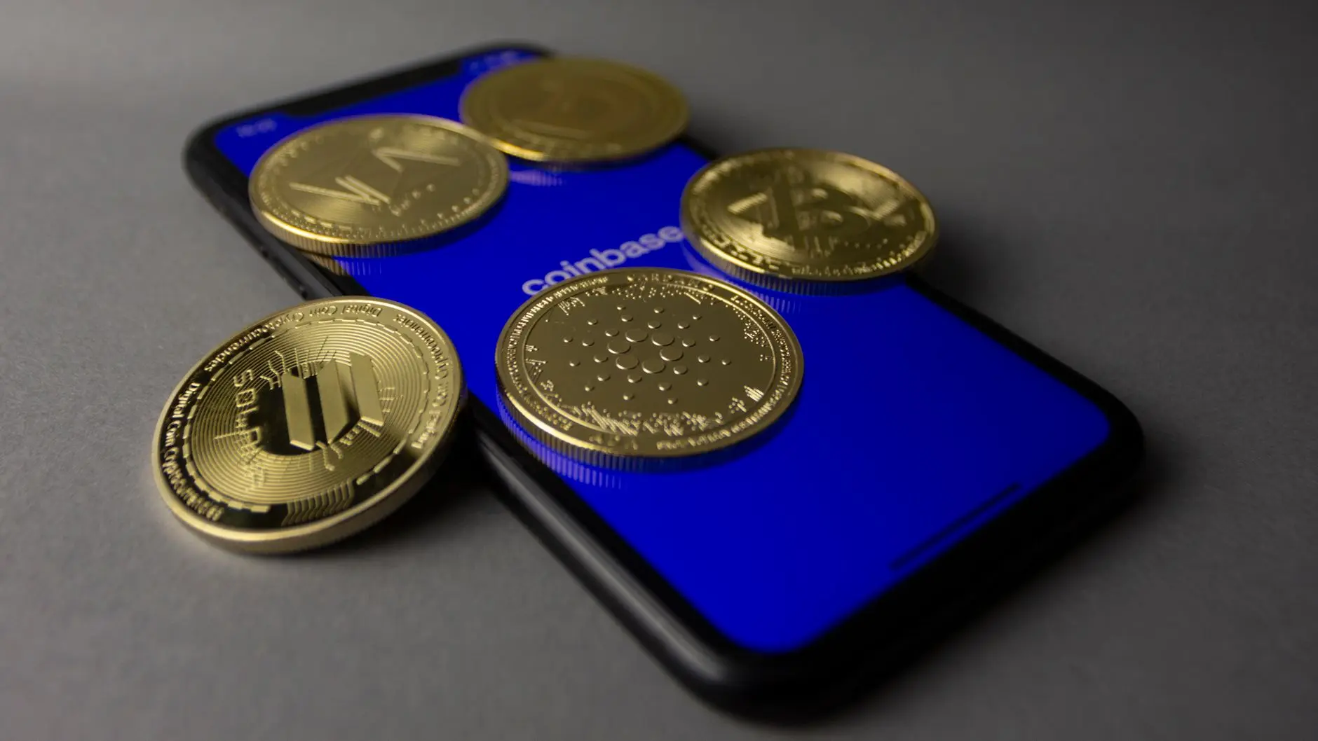 Gold cryptocurrency coins, including one with the Solana logo, resting on a smartphone showing the Coinbase app.