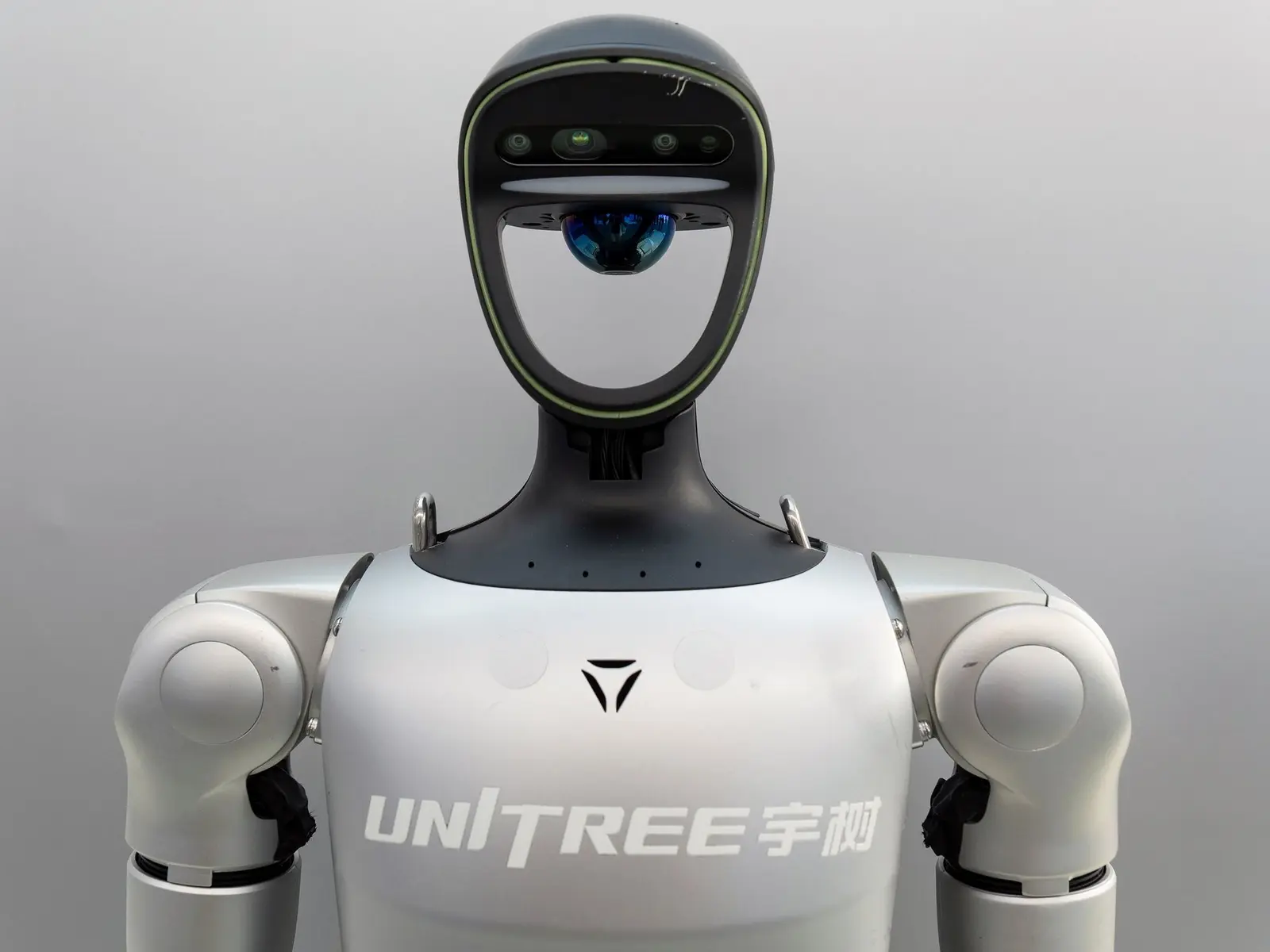 Close-up of a silver Unitree humanoid robot featuring a camera sensor in its head and the Unitree logo on its chest.