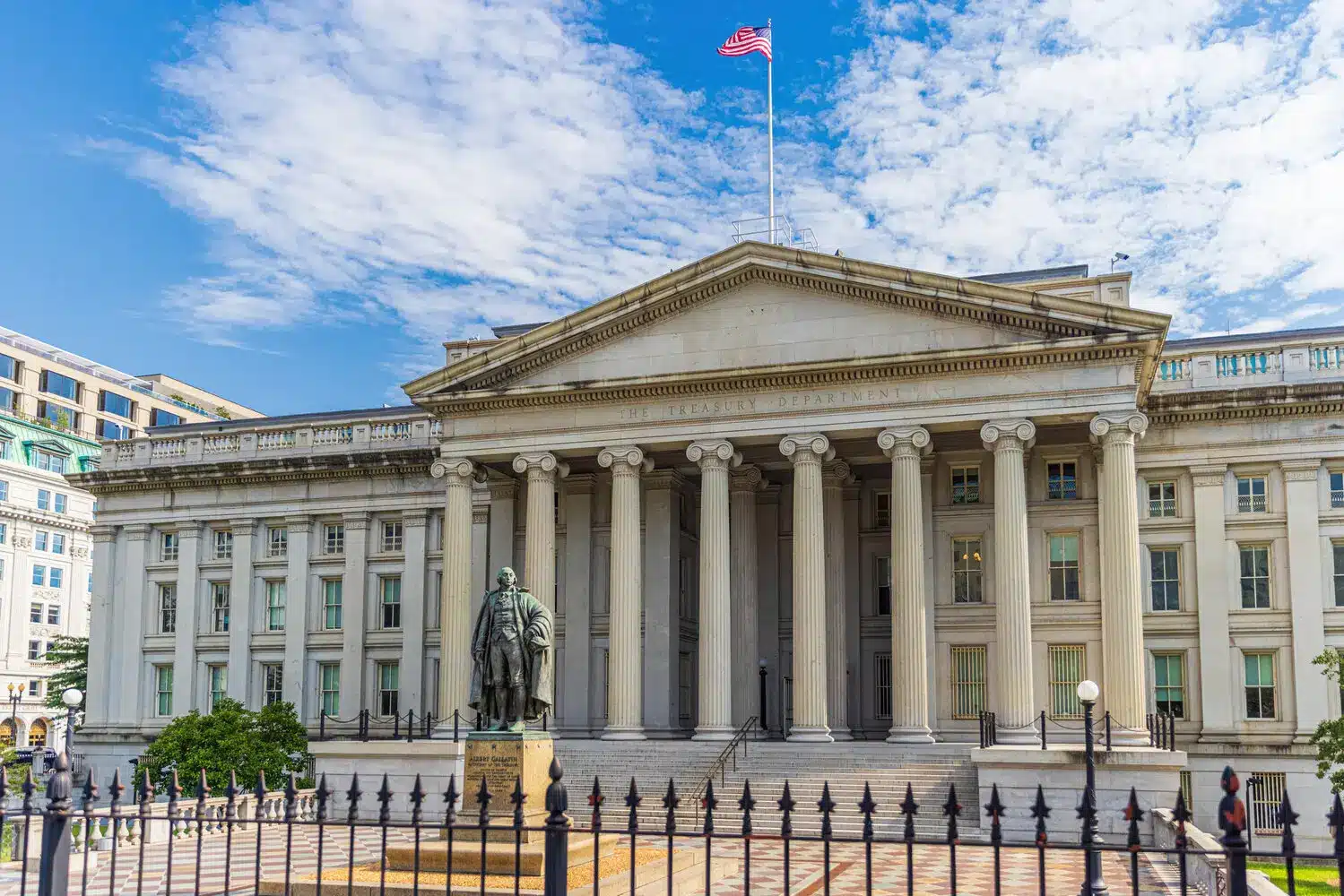 The neoclassical facade of the US Treasury Department building in Washington DC with a statue in the foreground.
