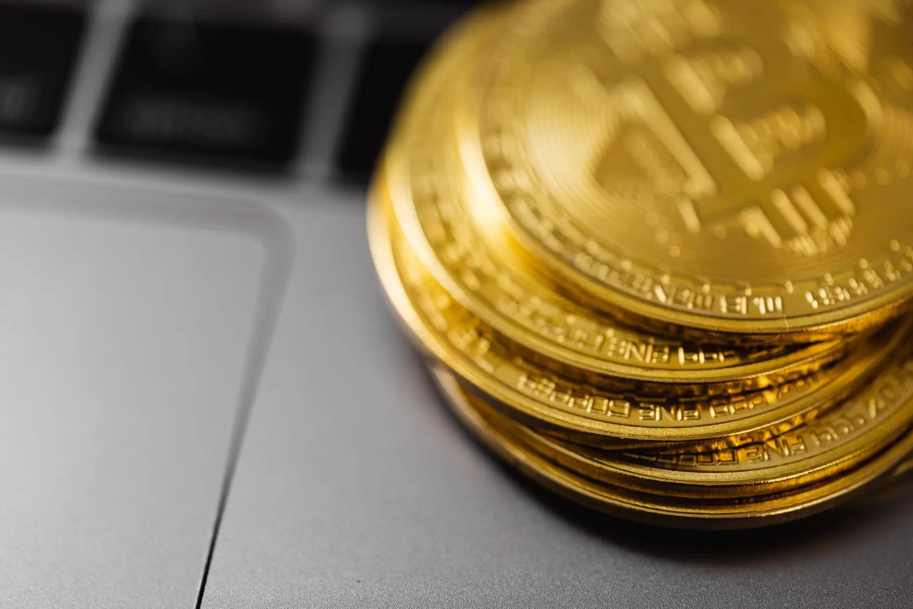 A stack of gold-colored Bitcoin tokens resting on the palm rest of a silver laptop
